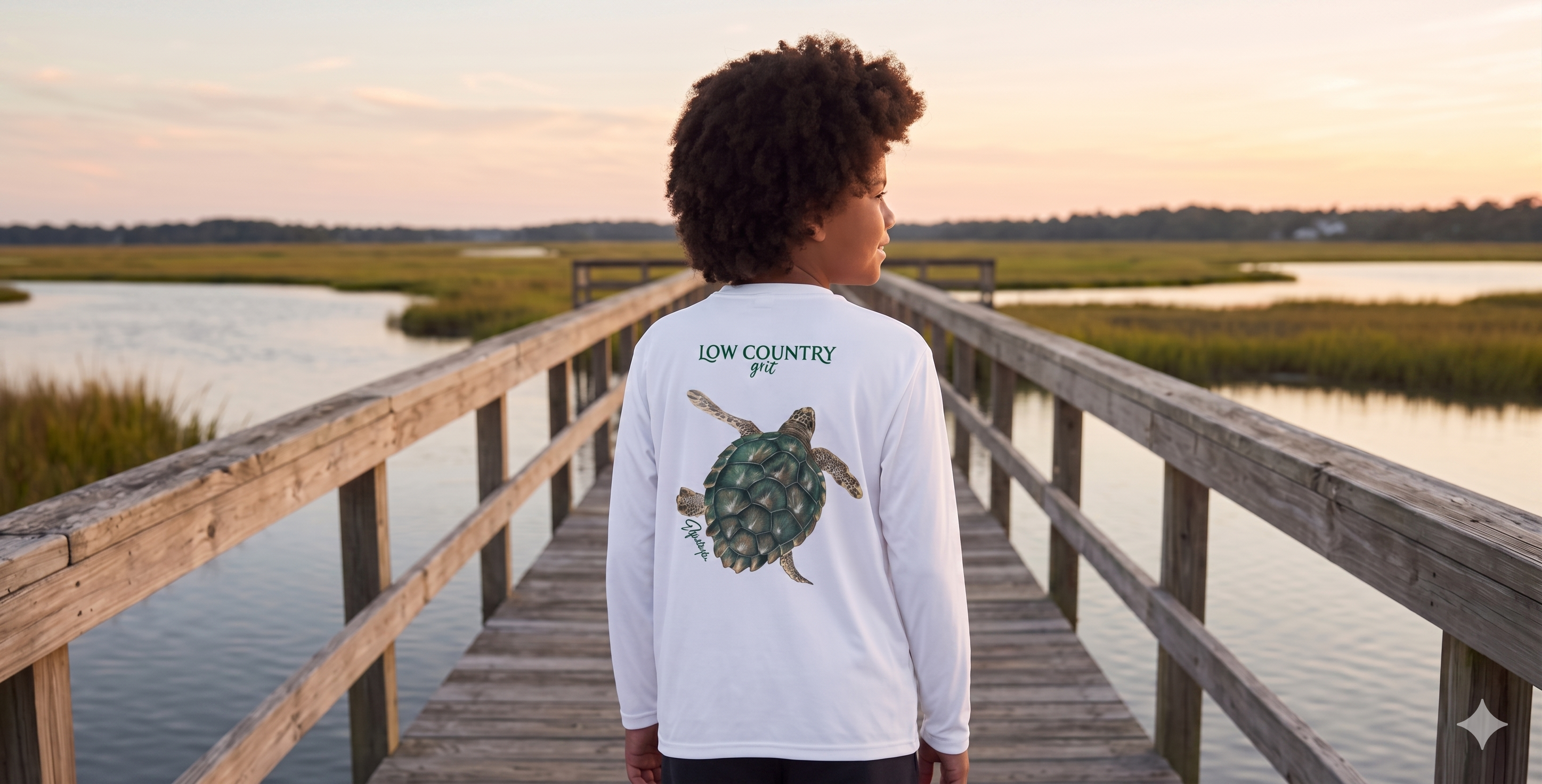 Person standing on a wooden dock by a body of water, wearing a white long-sleeve shirt with a turtle design.
